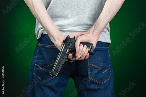 Firearms and murderer topic: man in a gray t-shirt holding a gun on a dark green background isolated in studio