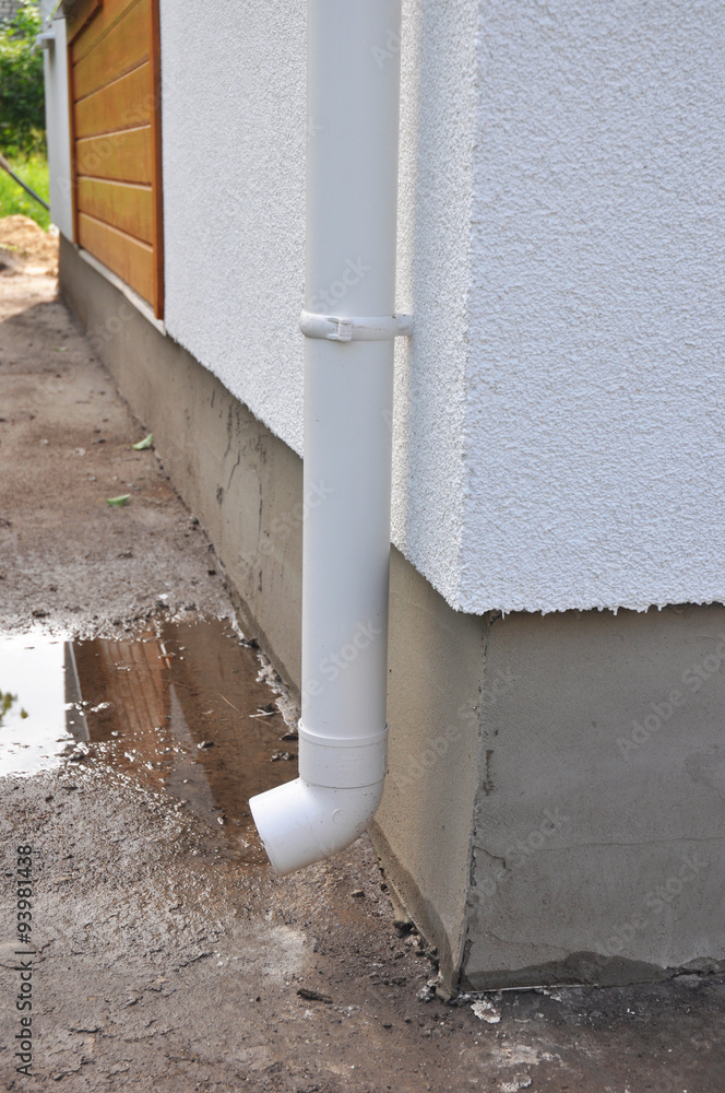 New rain gutter and downspouts on house construction with puddle. Close up on wet house foundation.