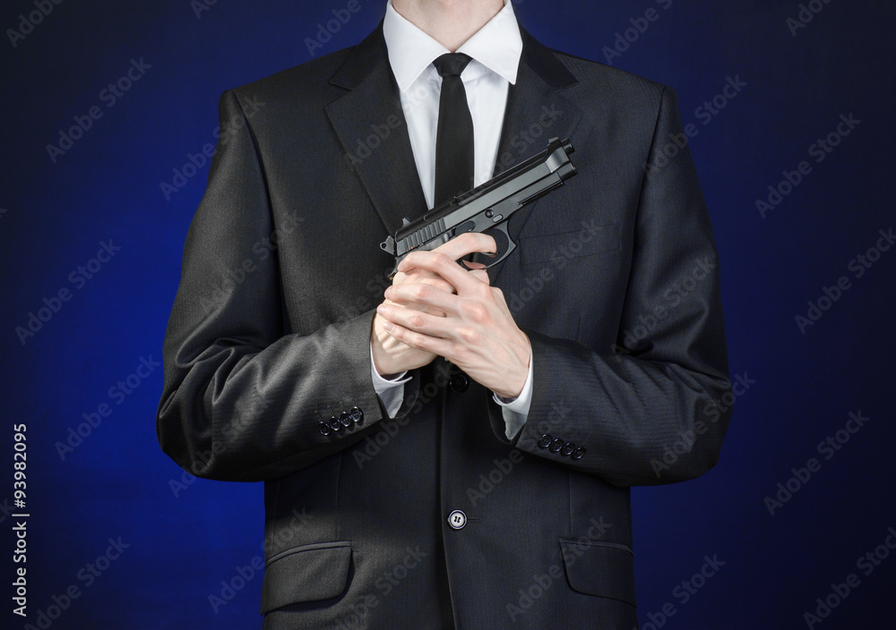 Firearms and security topic: a man in a black suit holding a gun on a dark blue background in studio isolated Firearms and security topic: a man in a black suit holding a gun on a dark blue background in studio isolated