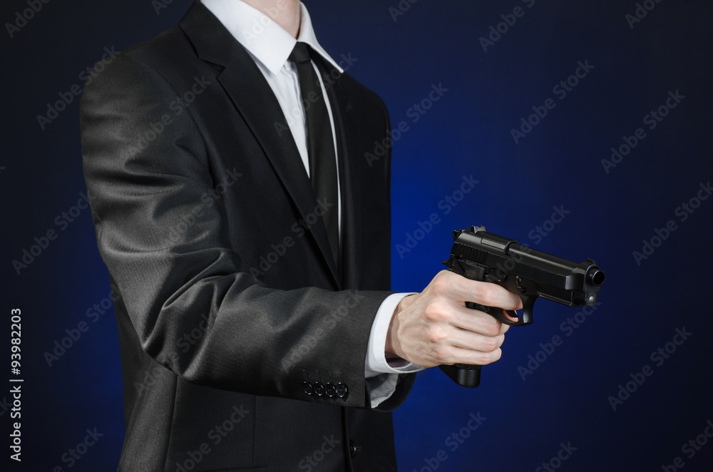Firearms and security topic: a man in a black suit holding a gun on a dark blue background in studio isolated Firearms and security topic: a man in a black suit holding a gun on a dark blue background in studio isolated