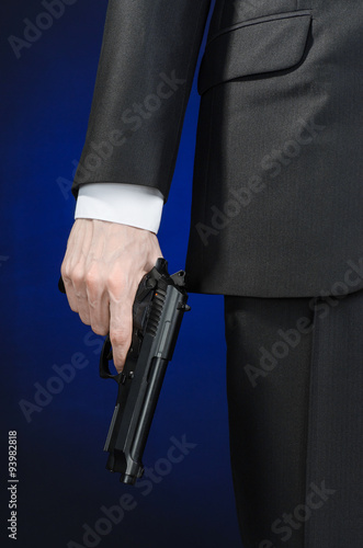 Firearms and security topic: a man in a black suit holding a gun on a dark blue background in studio isolated