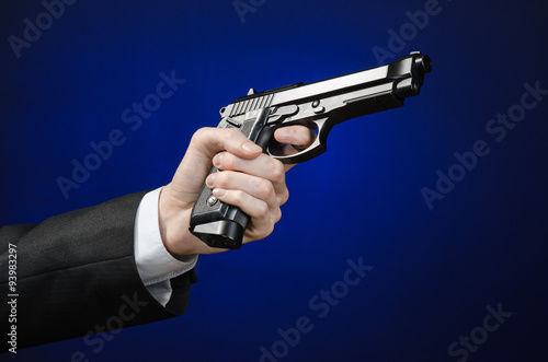 Firearms and security topic: a man in a black suit holding a gun on a dark blue background in studio isolated