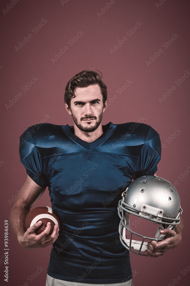 Confident american football player holding helmet and ball