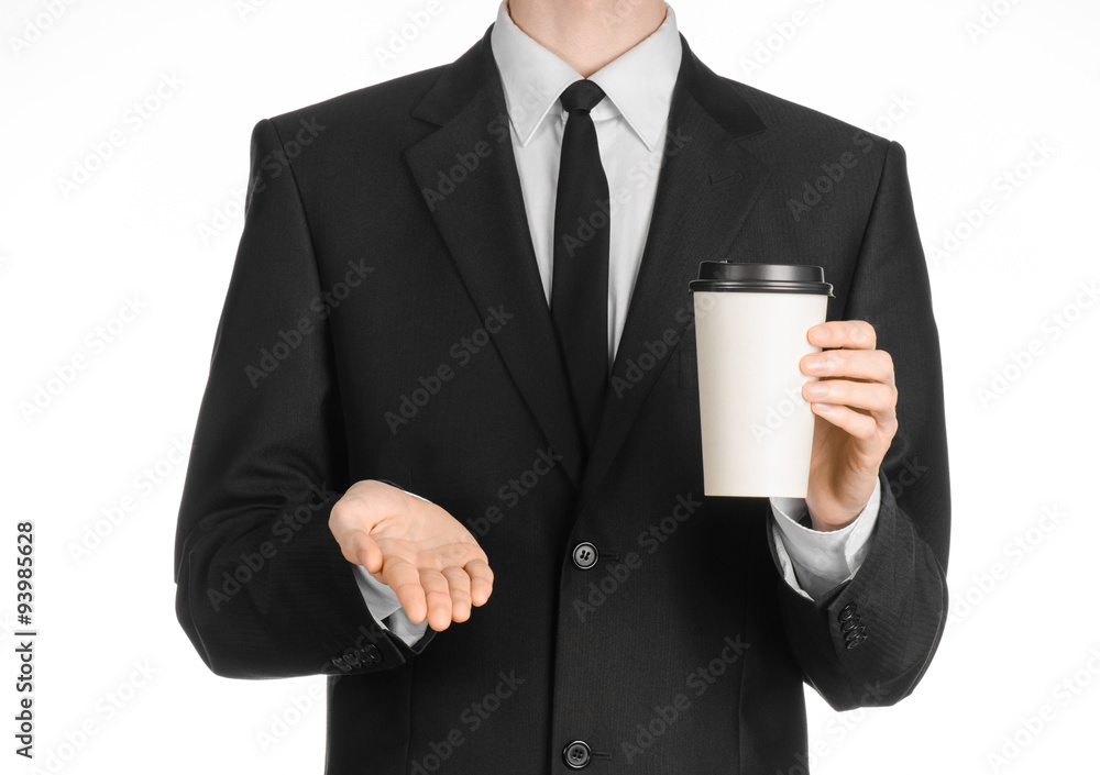 Business lunches coffee theme: businessman in a black suit holding a white blank paper cup of coffee with a brown plastic cap isolated on a white background in the studio, advertising coffee