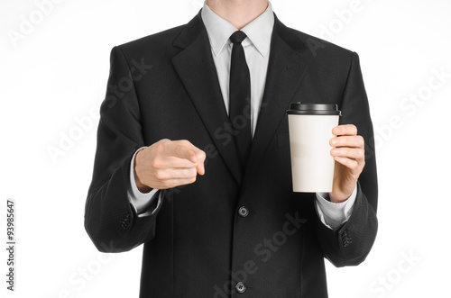 Business lunches coffee theme  businessman in a black suit holding a white blank paper cup of coffee with a brown plastic cap isolated on a white background in the studio  advertising coffee