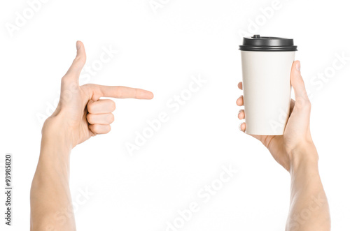 Breakfast and coffee theme: man's hand holding white empty paper coffee cup with a brown plastic cap isolated on a white background in the studio, advertising of coffee first-person view