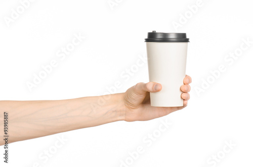 Breakfast and coffee theme: man's hand holding white empty paper coffee cup with a brown plastic cap isolated on a white background in the studio, advertising coffee