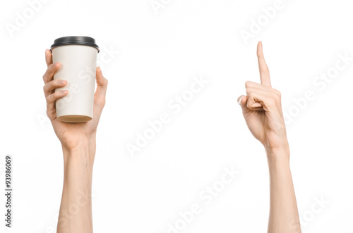 Breakfast and coffee theme: man's hand holding white empty paper coffee cup with a brown plastic cap isolated on a white background in the studio, advertising coffee