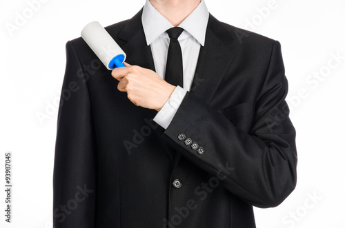 Dry cleaning and business theme: a man in a black suit holding a blue sticky brush for cleaning clothes and furniture from dust isolated on white background in studio.