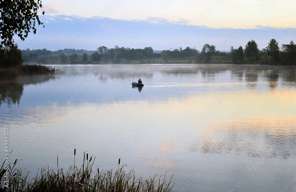 A fisherman in a boat sailing in the morning mist A fisherman in a boat sailing in the morning mist