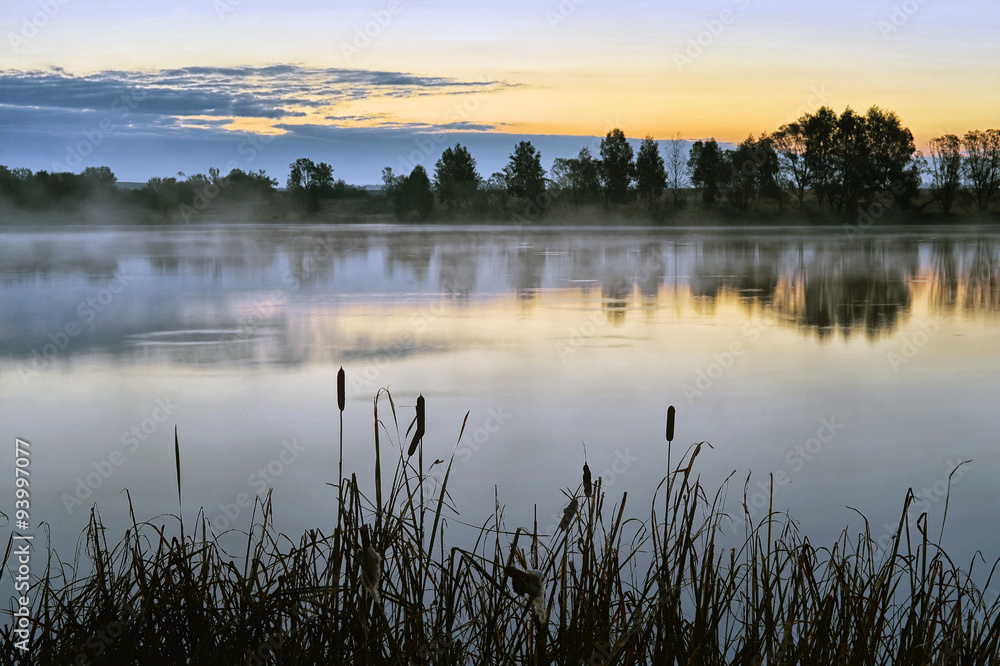 The morning landscape with sunrise over water in the fog