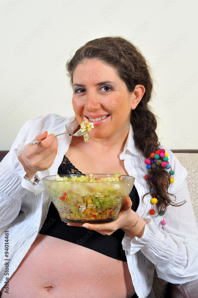 Pregnant woman sitting in living room with salad Pregnant woman sitting in living room with salad