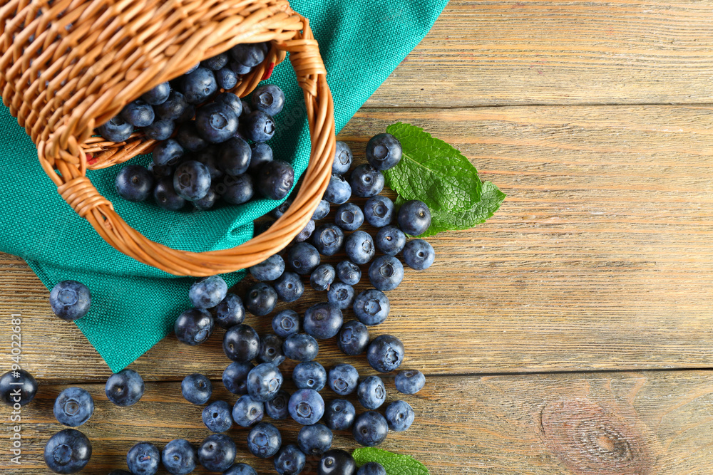 Tasty ripe blueberries with green leaves in basket on wooden table close up Tasty ripe blueberries with green leaves in basket on wooden table close up