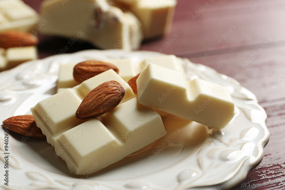 White chocolate pieces with nuts on plate, on color wooden background White chocolate pieces with nuts on plate, on color wooden background