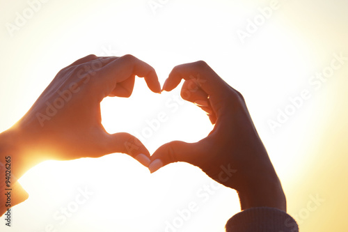 Hands in shape of love heart on sunlight background