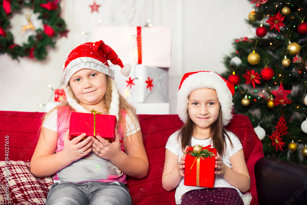 Two girls Christmas costumes sitting on the sofa with gifts in Two girls Christmas costumes sitting on the sofa with gifts in
