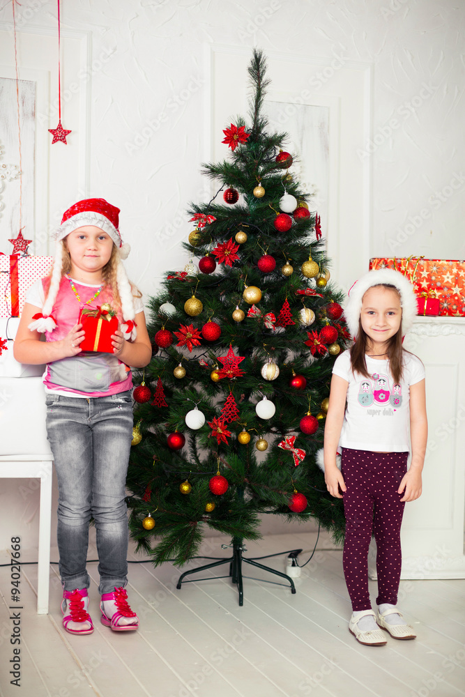 Two girls in Christmas costumes stand beside the tree with gifts Two girls in Christmas costumes stand beside the tree with gifts