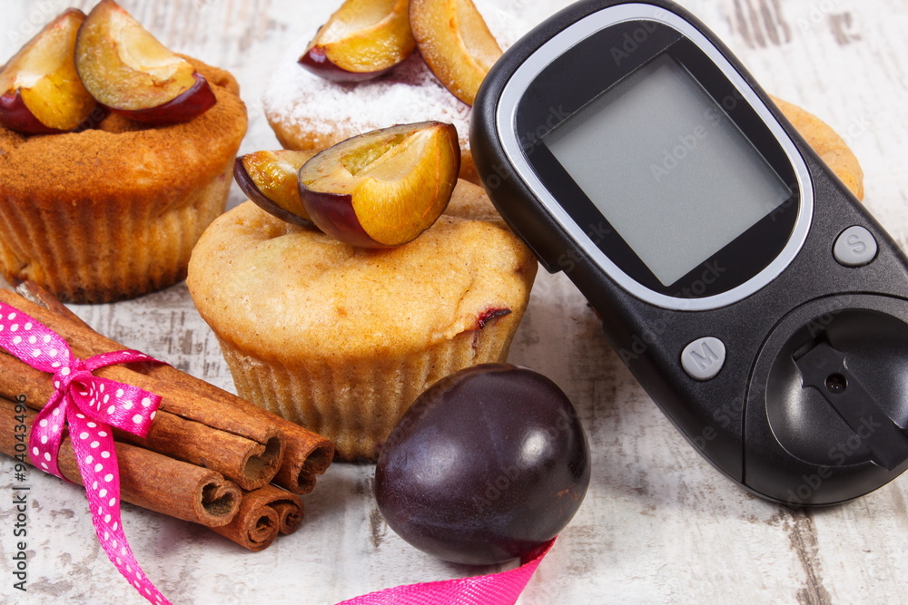 Glucometer, muffins with plums and cinnamon sticks on wooden background, diabetes and delicious dessert