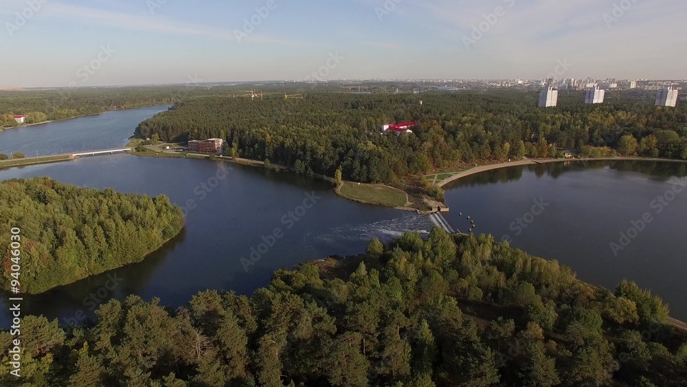 4K aerial view – flight over dam through the river with a green city district near 4K aerial view – flight over dam through the river with a green city district near