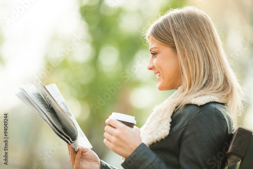 Young woman reading newspaper and drinking coffee to go