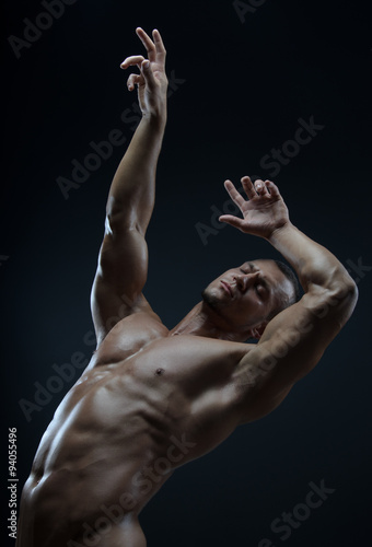 Bodybuilder and strip theme: beautiful with pumped muscles naked man posing in the studio on a dark background