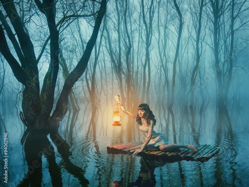 Fairy tale woman with lantern floating on the lake in the misty forest in rustic white dress.