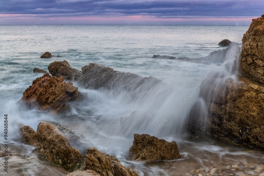 Splash and spray of waves against the rocks. Sunset on the sea.