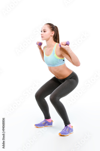 Young sportswoman squatting with dumbbells