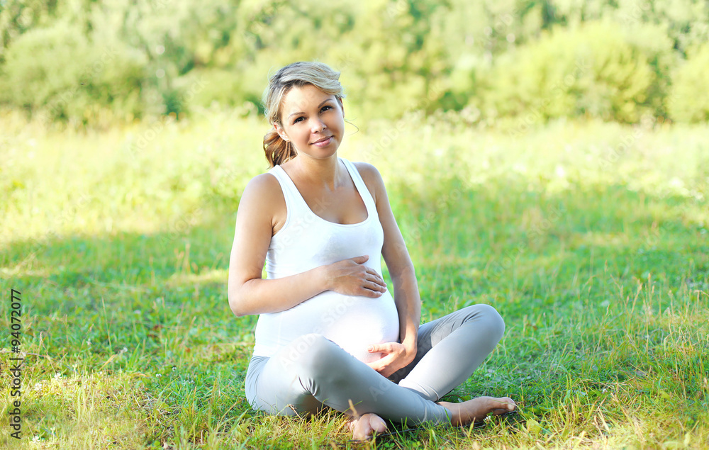 Happy young pregnant woman sitting on grass doing yoga Happy young pregnant woman sitting on grass doing yoga
