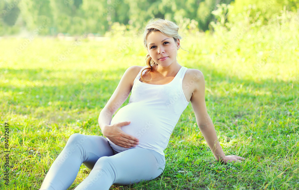 Young pregnant woman sitting on grass in summer sunny day Young pregnant woman sitting on grass in summer sunny day