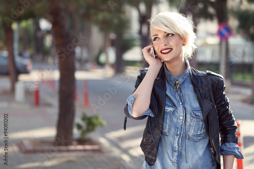 portrait of a young punk style blond woman outdoor, talking with her mobile phone