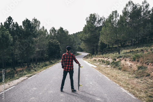 Man riding on a longboard skate on a road through a forest photo