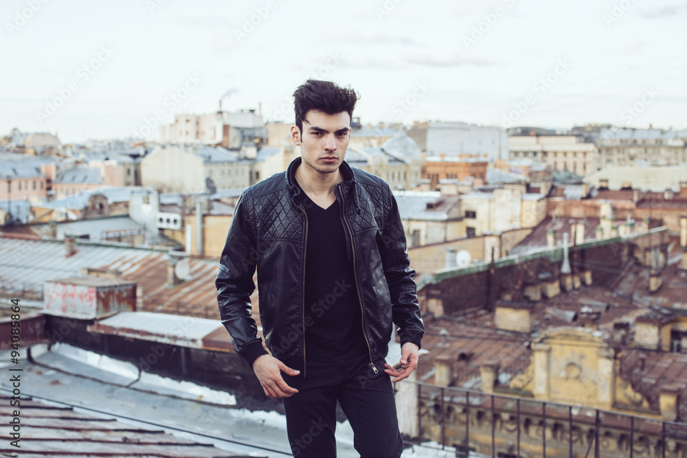 Man in a leather jacket on a rooftop in the center of the city