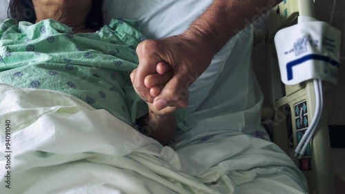 Man's hands holding woman's hands as she lays down in hospital bed