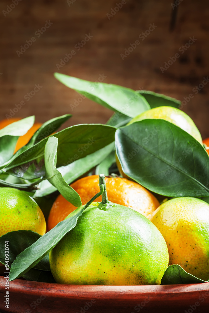 Orange and green ripe tangerines with leaves on a clay plate on