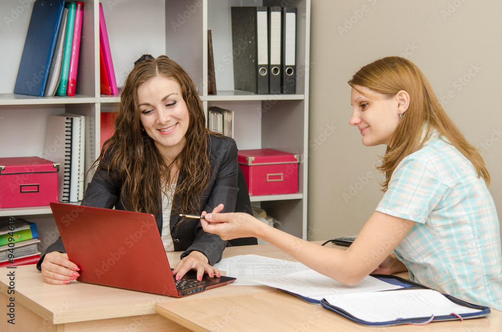 Two employees of the office happily look into the laptop discussing documents Two employees of the office happily look into the laptop discussing documents