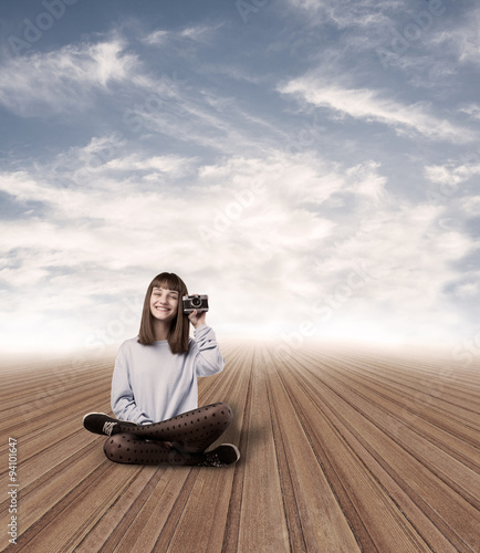 young woman holding a camera sitting on a wooden floor at abstra photo