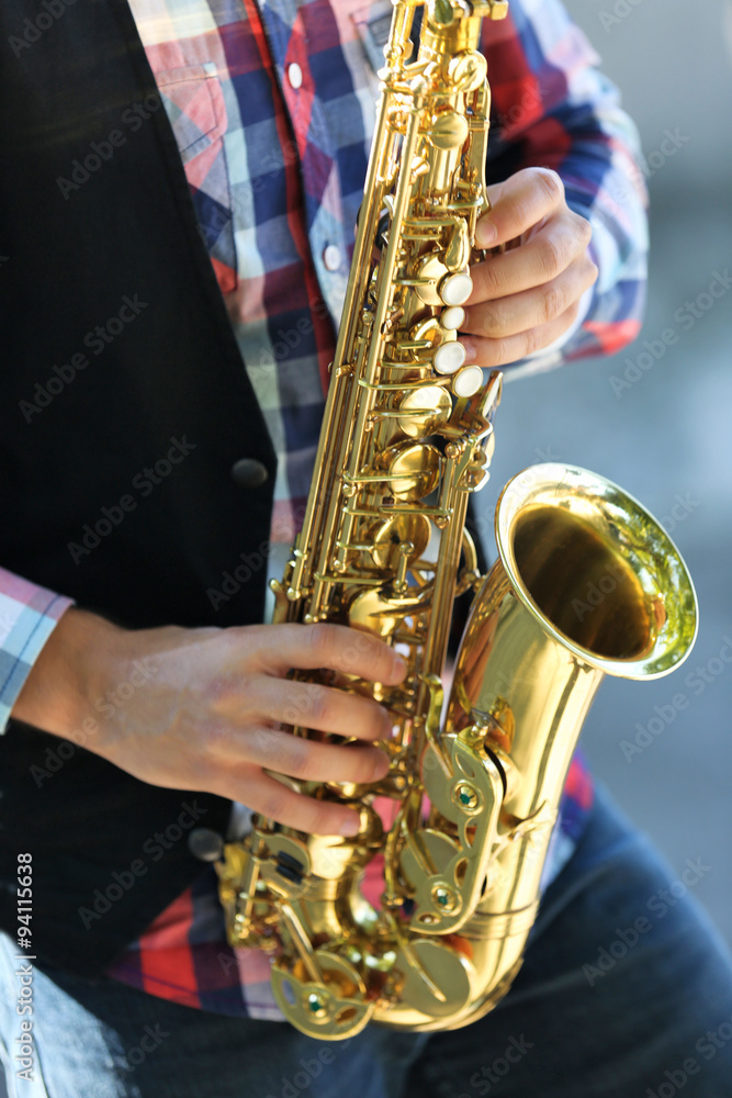 Obraz premium Handsome young man plays sax outdoors, close up