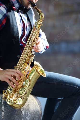Handsome young man plays sax outdoors, close up