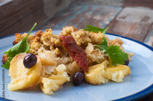 Bacalhau broa. A Portuguese Brazilian dish of salt cod baked with crumbled corn bread, olive oil and olives. Garnished with sun dried tomatoes and parsley.