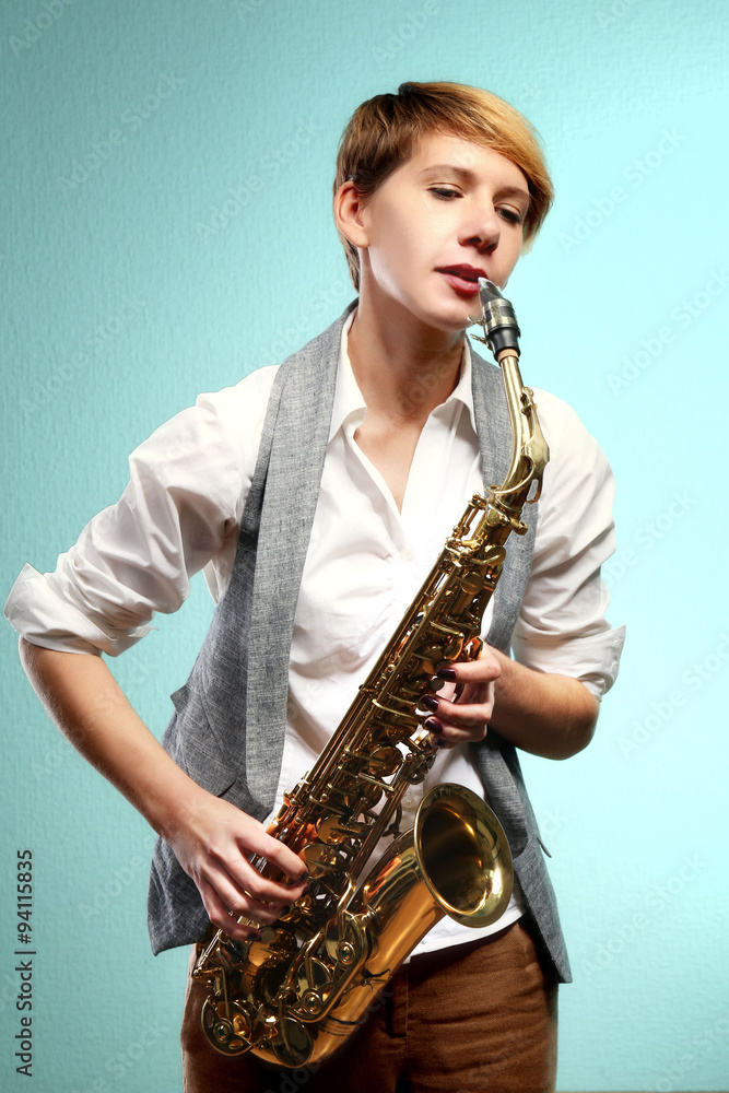 Fototapeta premium Pretty woman plays music on saxophone in front of blue background