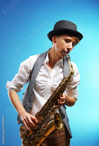 Pretty woman plays music on saxophone in front of blue background