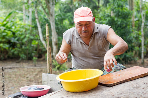 Rural chef expertly preparing lunch outdoors seated against a backdrop of lush vegetation showcasing authentic culinary skills in a natural setting