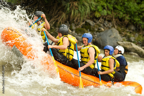 A team of adventurers in helmets navigating white rapids on a raft in Ecuador, surrounded by rocks and the rush of extreme whitewater action. © Ammit