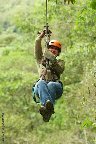 A woman soaring through the canopy on a zipline over crystal clear agua, with lush green trees lining the zip line path.