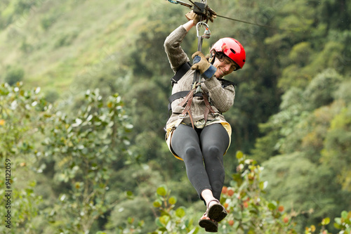 A woman ziplining through the lush forest canopy in Baños de Agua Santa, Ecuador on a thrilling adventure sliding down a wire rope.