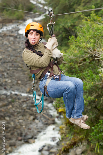 An extremely ugly woman wearing a helmet ziplining on a wire with other women in the background.