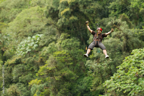 A group of people zip lining through the lush canopy of an Ecuadorian rainforest, surrounded by towering trees and vibrant green foliage.