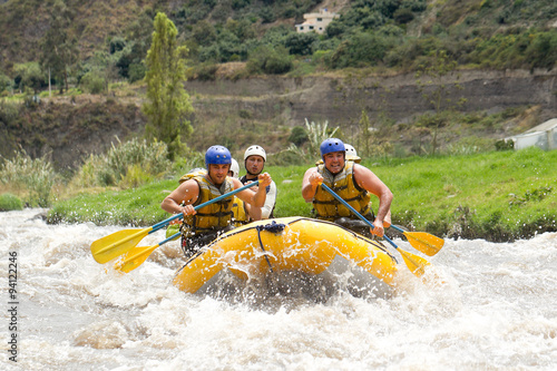 A group of teenagers in a white raft shoot through powerful rapids with their instructor, surrounded by nature's beauty on an extreme water sport adventure.