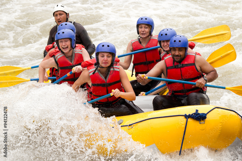 A group of adventurous people in helmets and life jackets navigating a white water rafting adventure with their experienced guide team on a rushing river.
